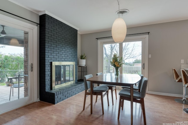 dining space featuring a brick fireplace, visible vents, wood finished floors, and ornamental molding