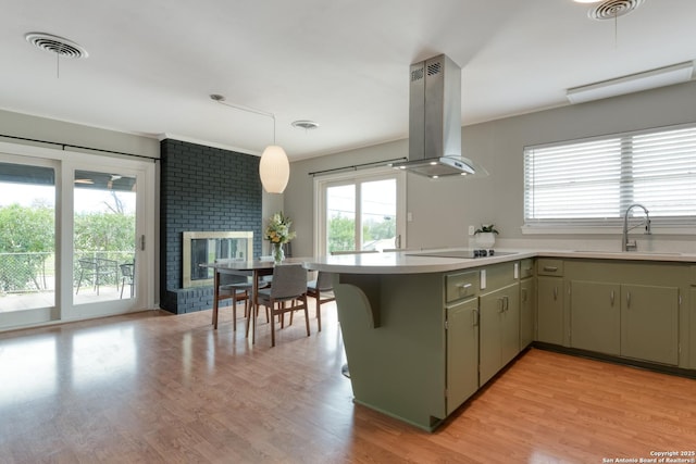 kitchen with black electric stovetop, island range hood, a fireplace, a sink, and light wood-style floors