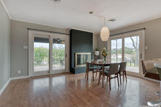 dining room featuring a brick fireplace, wood finished floors, visible vents, and baseboards