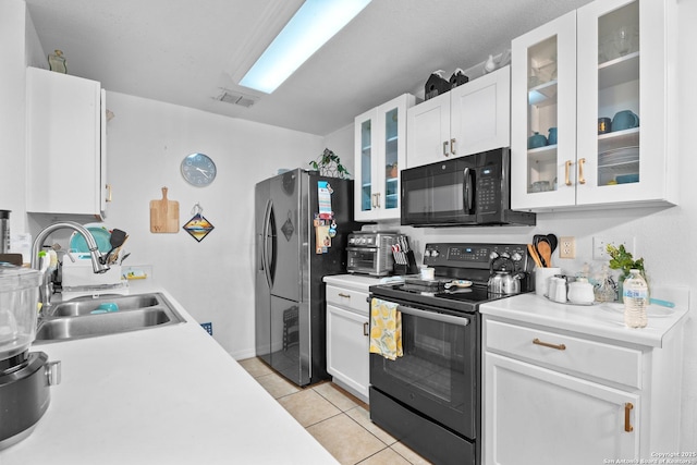 kitchen featuring sink, light tile patterned floors, black appliances, and white cabinets