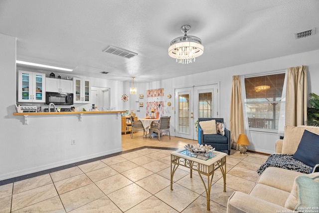 living room with french doors, sink, a textured ceiling, light tile patterned floors, and a notable chandelier