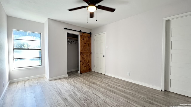 unfurnished bedroom with ceiling fan, a barn door, and light wood-type flooring