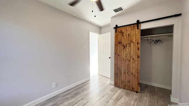 unfurnished bedroom with ceiling fan, a barn door, a closet, and light hardwood / wood-style flooring