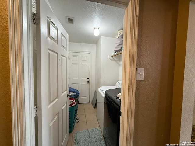 washroom featuring light tile patterned flooring, washing machine and clothes dryer, and a textured ceiling