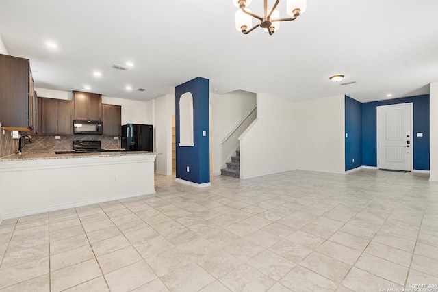 kitchen featuring sink, decorative backsplash, light stone counters, black appliances, and an inviting chandelier