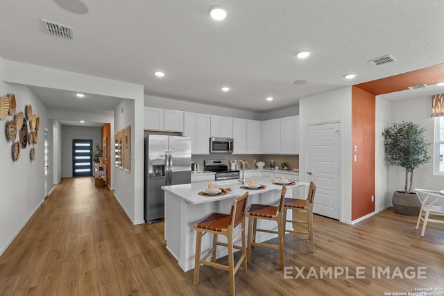 kitchen featuring a breakfast bar, white cabinetry, stainless steel appliances, an island with sink, and light wood-type flooring