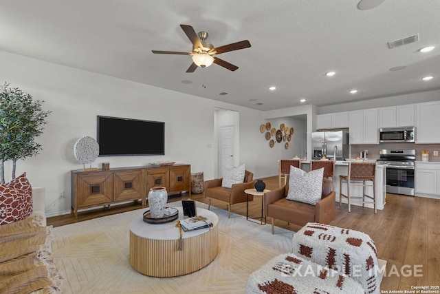 living room with a textured ceiling, ceiling fan, and light wood-type flooring