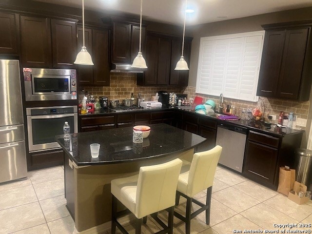 kitchen with sink, appliances with stainless steel finishes, backsplash, a kitchen breakfast bar, and a center island