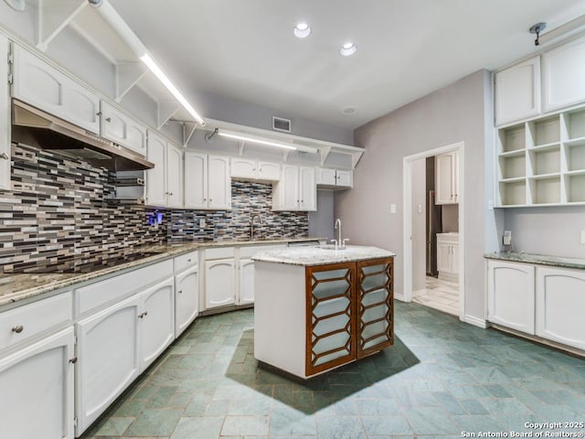 kitchen with sink, white cabinetry, light stone countertops, an island with sink, and black electric cooktop