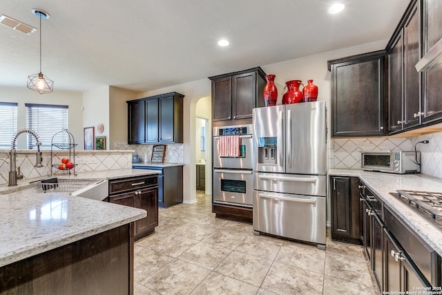 kitchen with dark brown cabinetry, sink, light stone counters, hanging light fixtures, and stainless steel appliances