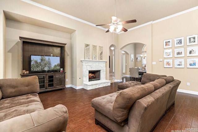 living room featuring crown molding, a stone fireplace, and ceiling fan with notable chandelier