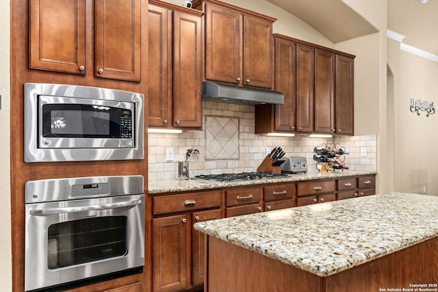 kitchen with light stone counters, decorative backsplash, stainless steel appliances, and lofted ceiling