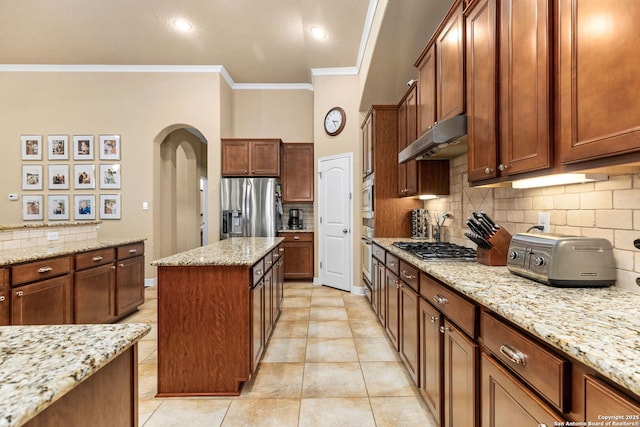 kitchen featuring appliances with stainless steel finishes, a center island, light stone counters, tasteful backsplash, and ornamental molding