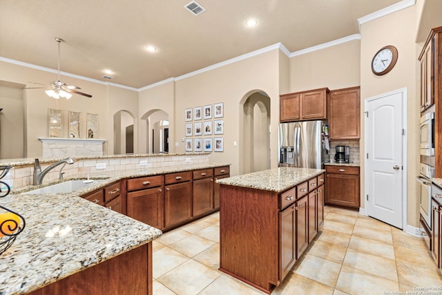 kitchen with a kitchen island, appliances with stainless steel finishes, sink, decorative backsplash, and light stone countertops