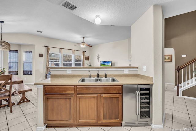 kitchen with light tile patterned flooring, pendant lighting, sink, beverage cooler, and a textured ceiling