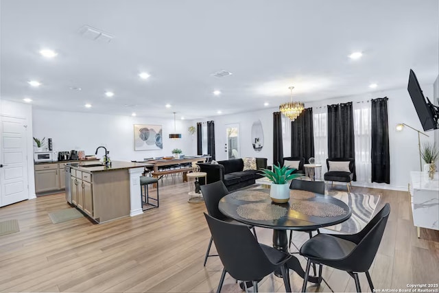 dining room with sink, a chandelier, and light wood-type flooring