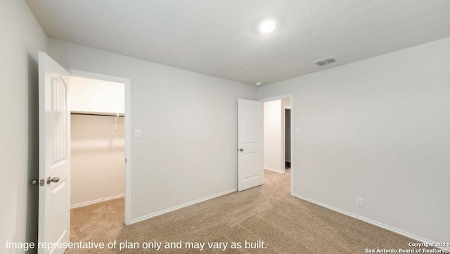 unfurnished bedroom featuring a walk in closet, light carpet, and a closet