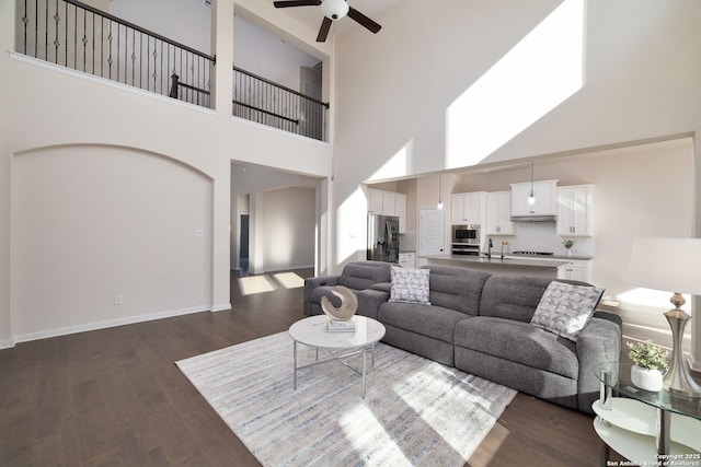 living room featuring ceiling fan, a towering ceiling, sink, and dark hardwood / wood-style flooring