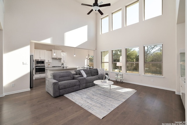 living room with a high ceiling, dark wood-type flooring, and ceiling fan with notable chandelier