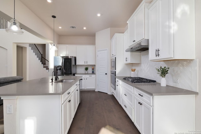 kitchen with white cabinetry, backsplash, stainless steel appliances, a center island with sink, and decorative light fixtures