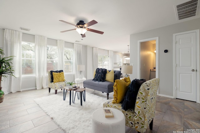 living room with a ceiling fan, visible vents, and baseboards