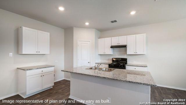 kitchen with sink, black gas range, light stone countertops, an island with sink, and white cabinets