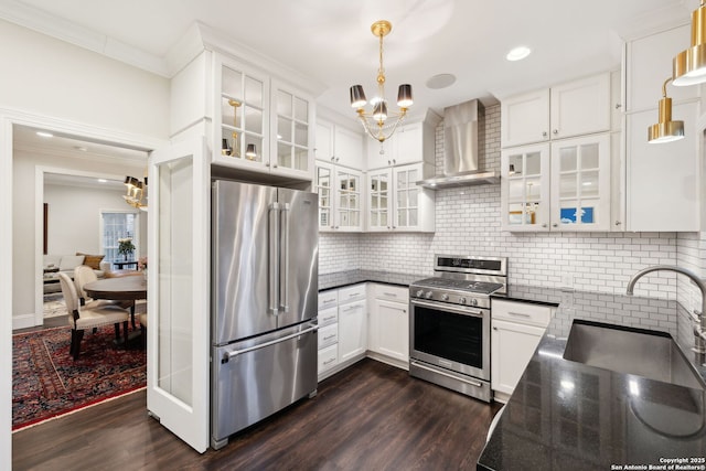 kitchen featuring appliances with stainless steel finishes, pendant lighting, white cabinetry, backsplash, and wall chimney exhaust hood