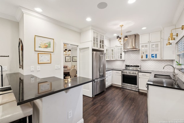 kitchen featuring wall chimney range hood, a breakfast bar, appliances with stainless steel finishes, hanging light fixtures, and kitchen peninsula