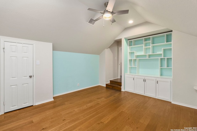 additional living space featuring built in shelves, vaulted ceiling, light hardwood / wood-style floors, and ceiling fan