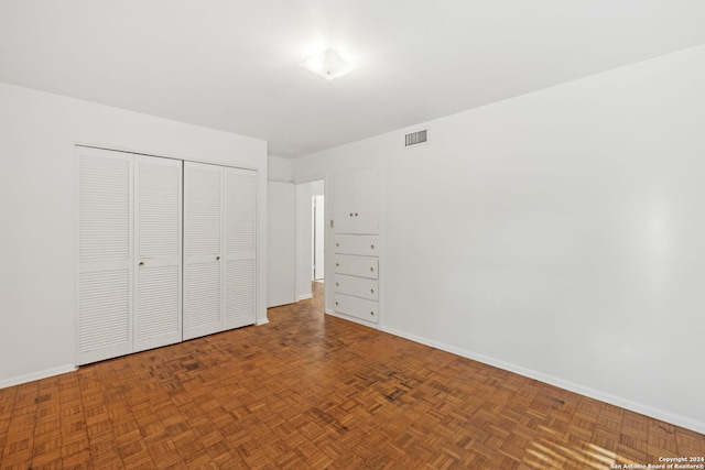 unfurnished bedroom featuring parquet floors and a closet