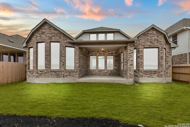 back of house at dusk with fence private yard, a patio area, brick siding, and a lawn