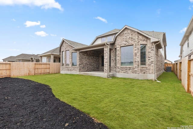 back of house with brick siding, a yard, a fenced backyard, and a patio