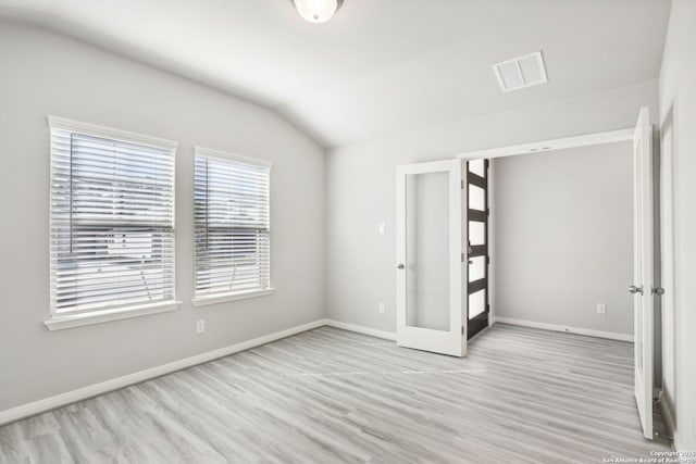 spare room with lofted ceiling, light hardwood / wood-style floors, and french doors