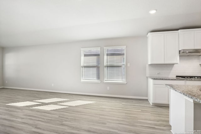 kitchen with light hardwood / wood-style flooring, tasteful backsplash, light stone countertops, stainless steel gas cooktop, and white cabinets