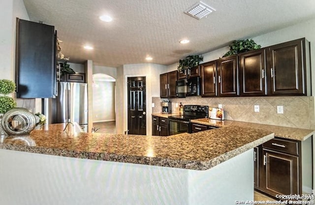 kitchen featuring kitchen peninsula, backsplash, dark brown cabinetry, and black appliances