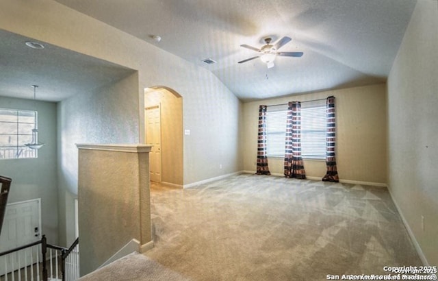 carpeted empty room with ceiling fan, vaulted ceiling, and a textured ceiling