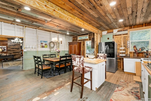 kitchen with stainless steel refrigerator with ice dispenser, hanging light fixtures, light hardwood / wood-style flooring, a kitchen island, and white cabinets