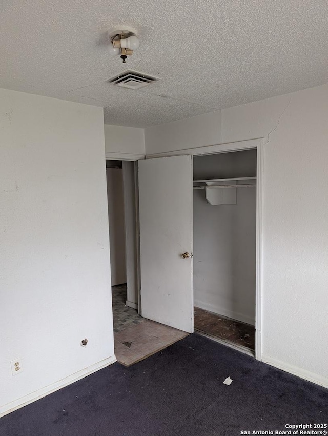 unfurnished bedroom featuring a closet, dark carpet, and a textured ceiling