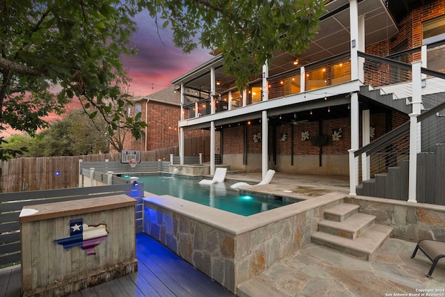 pool at dusk featuring a patio area, pool water feature, an outdoor bar, and a deck