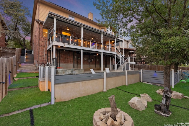 back house at dusk with a wooden deck, a fire pit, and a lawn