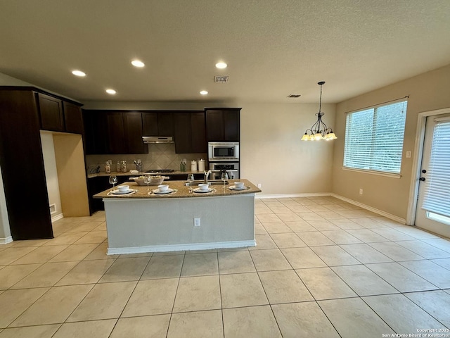 kitchen featuring light tile patterned flooring, appliances with stainless steel finishes, light stone countertops, and an island with sink