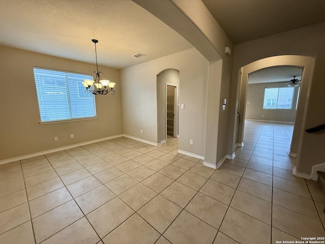 tiled empty room with ceiling fan with notable chandelier