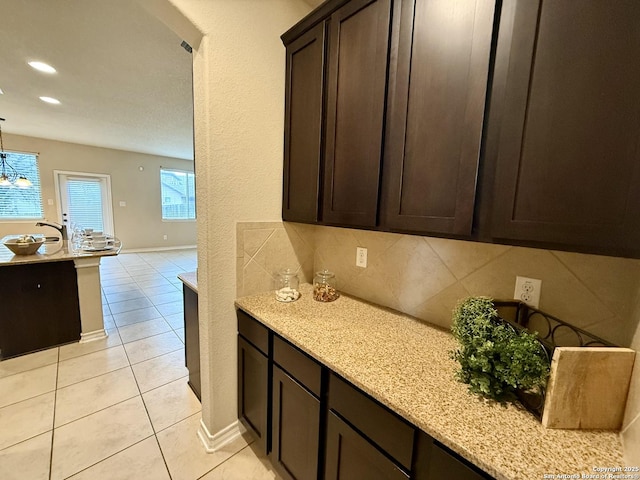 kitchen featuring light stone counters, light tile patterned floors, decorative light fixtures, and dark brown cabinetry