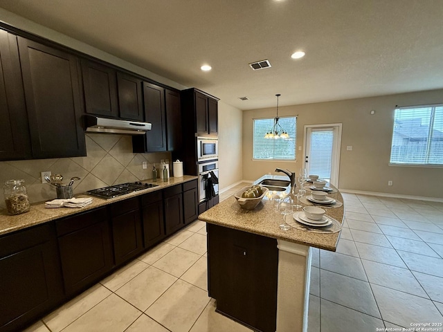 kitchen featuring sink, hanging light fixtures, appliances with stainless steel finishes, an island with sink, and decorative backsplash