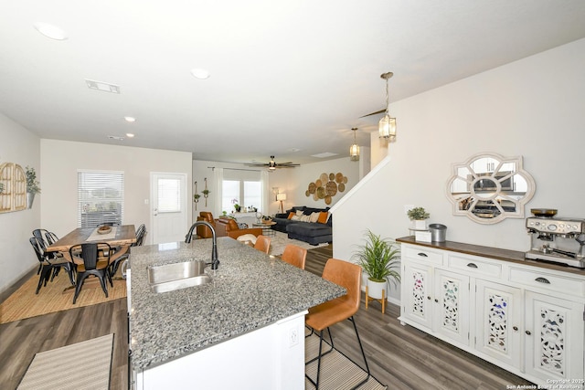 kitchen with sink, a breakfast bar area, white cabinets, dark hardwood / wood-style flooring, and dark stone counters