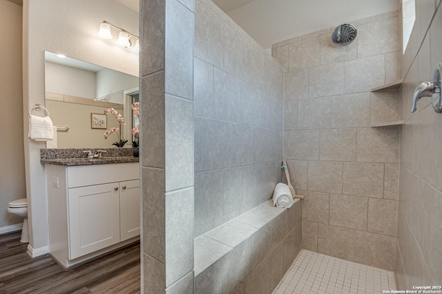 bathroom featuring vanity, tiled shower, hardwood / wood-style floors, and toilet