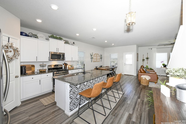 kitchen with appliances with stainless steel finishes, white cabinetry, sink, dark stone countertops, and dark hardwood / wood-style flooring