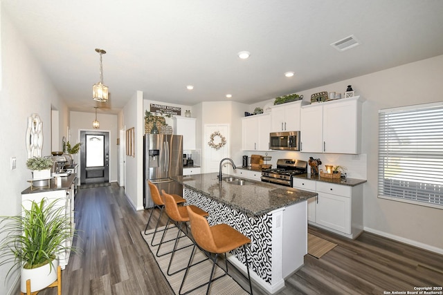 kitchen featuring sink, white cabinetry, hanging light fixtures, stainless steel appliances, and an island with sink