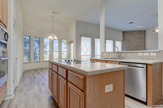 kitchen featuring sink, appliances with stainless steel finishes, a center island, light hardwood / wood-style floors, and decorative backsplash