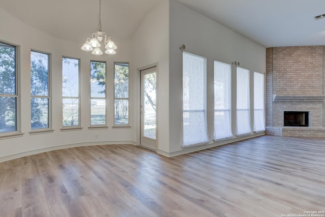 unfurnished living room with a brick fireplace, a chandelier, and light hardwood / wood-style floors